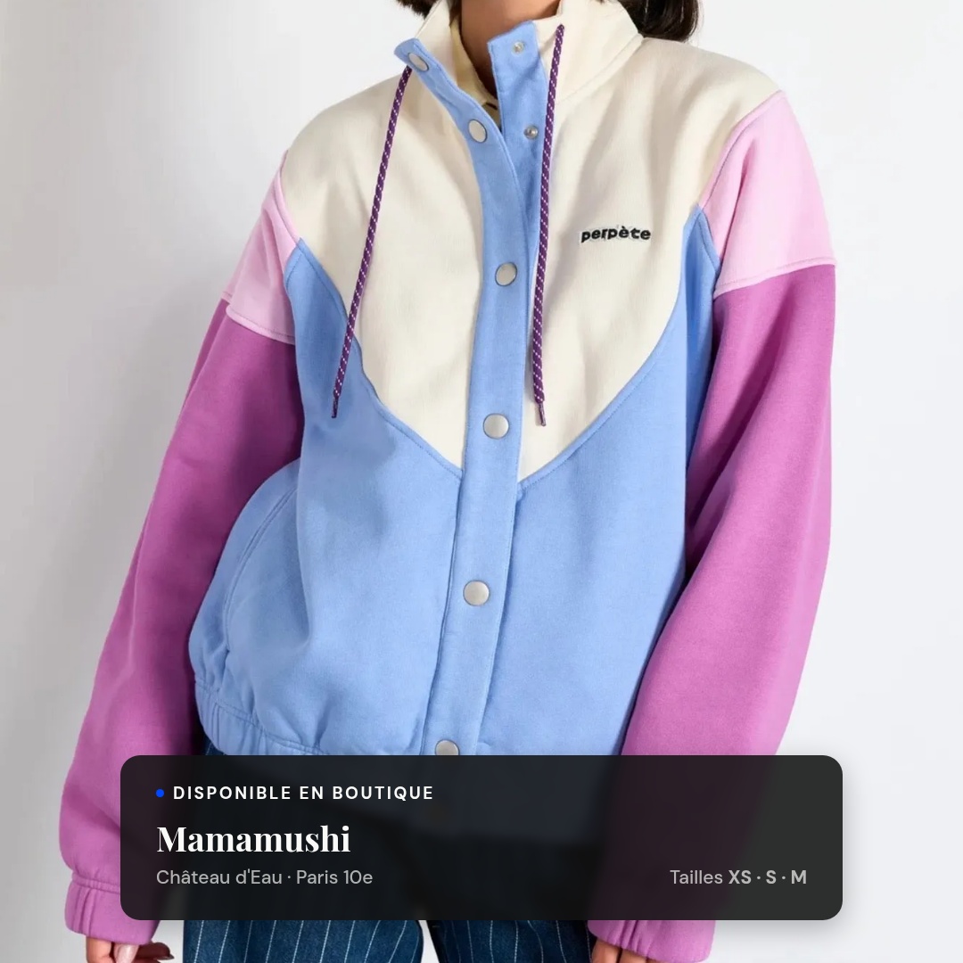 Veste colorblock Perpète bleu ciel, écru et lilas, à col montant et cordon violet, portée de face, cadrage faceless du menton à la taille, fond neutre. Encart en bas de l'image : pastille « Disponible en boutique », nom de la boutique Mamamushi, quartier Château d'Eau — Paris 10e, tailles XS · S · M.